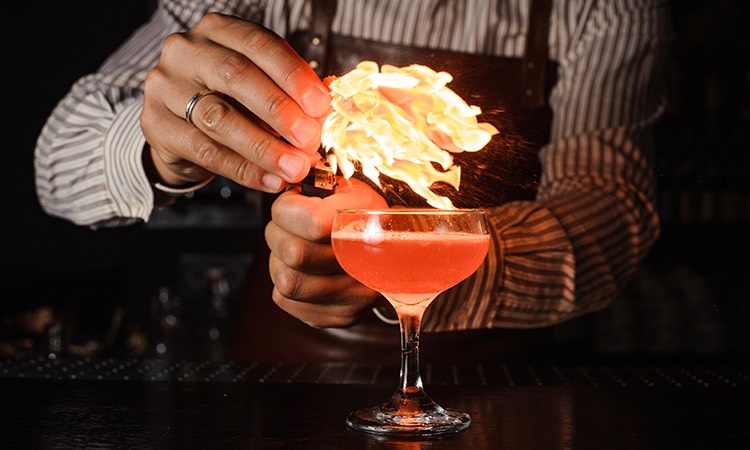bartender putting a flaming garnish in a pink cocktail drink