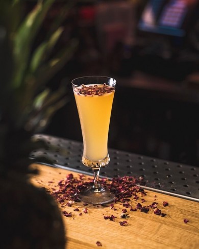 a cocktail on a bar garnished with crushed purple leaves