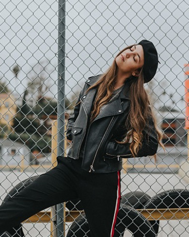 a girl in a leather jacket leaning against a chain link fence