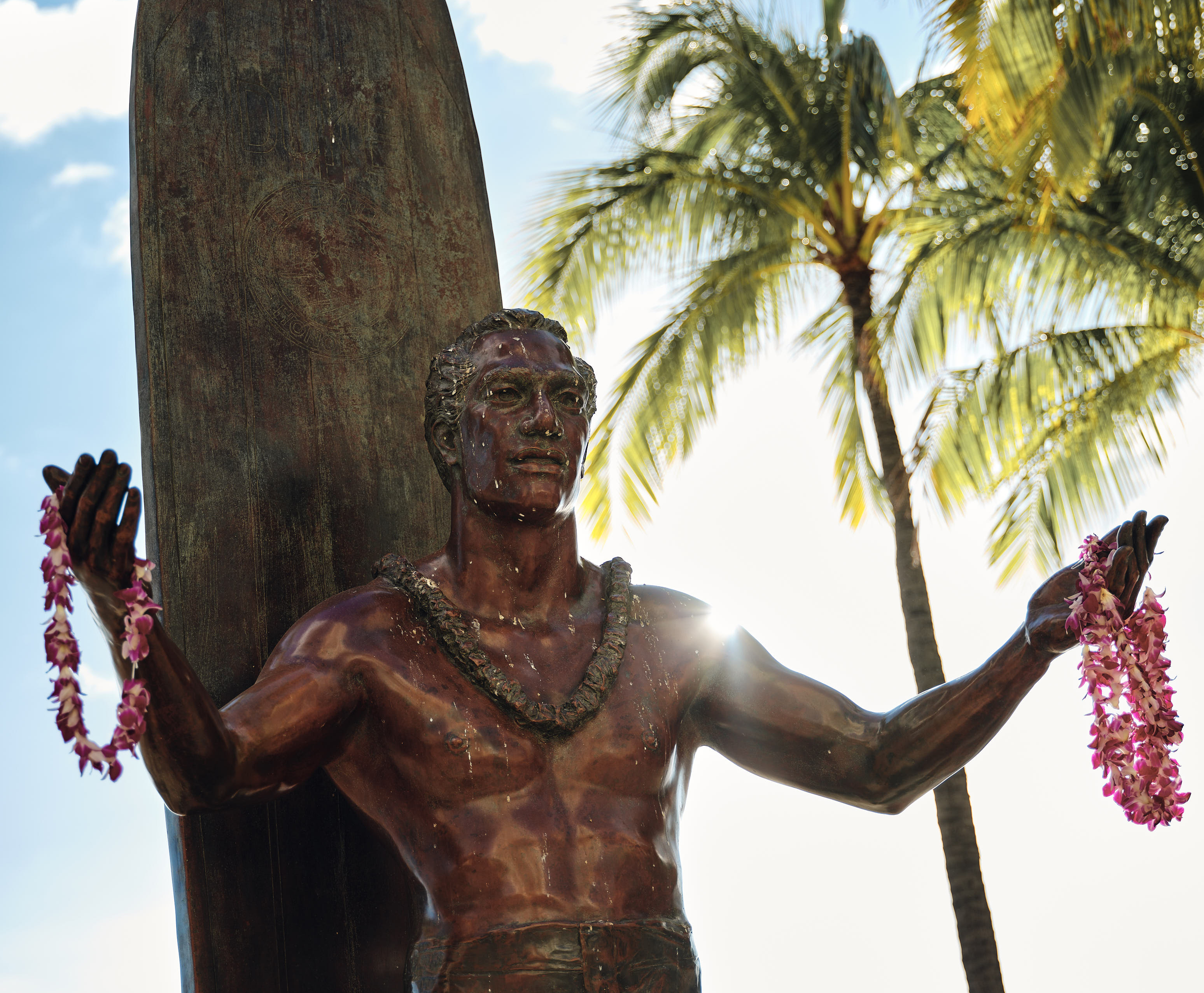 hawaiian sculpture holding flower collars with palm trees on the background