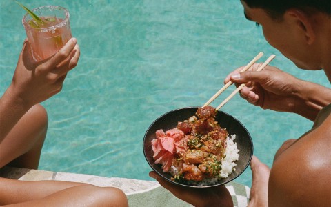 a man holding chopsticks with tuna from a poke bowl next to a woman holding a glass 