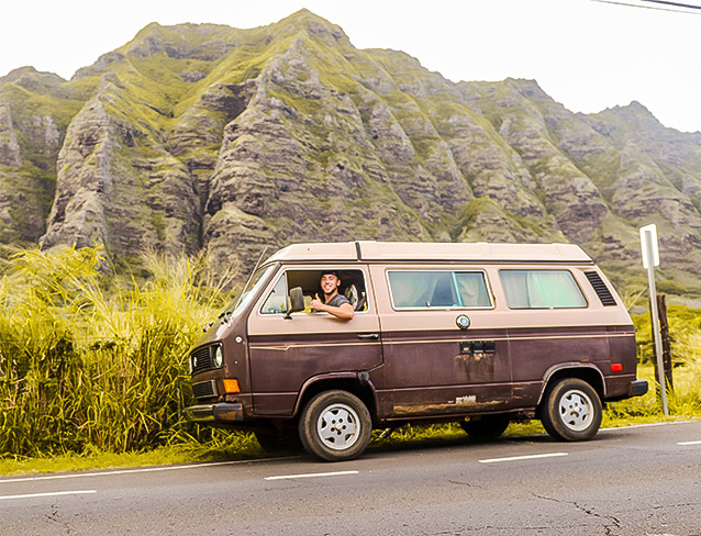 man driving a van with the Hawaiian mountains in the background 