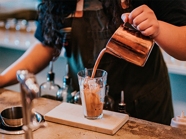 a barista pouring coffee on a glass with ice