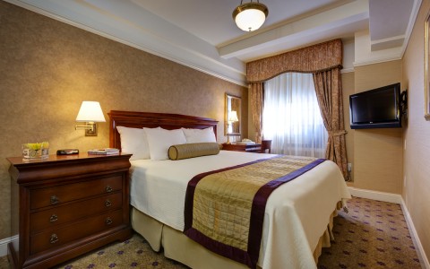 hotel bed with beige throw blanket and beige curtains
