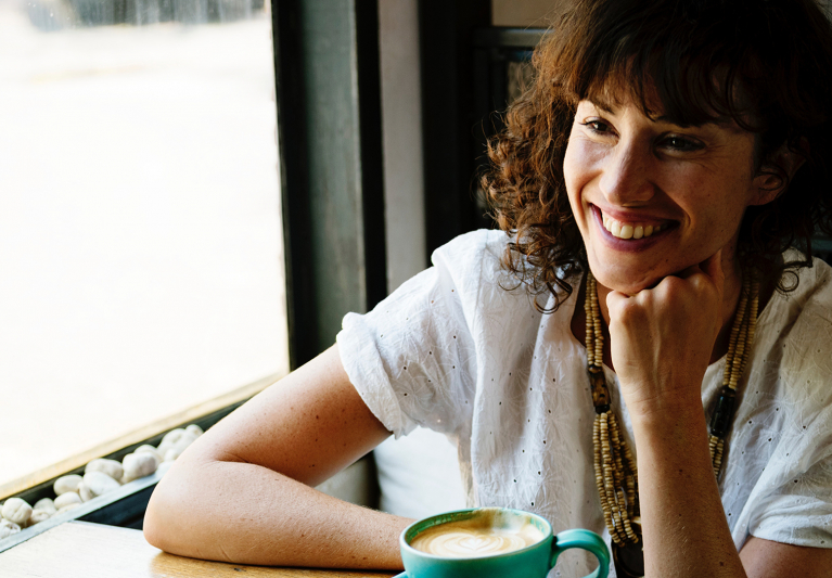 Woman smiling at table with coffee next to window