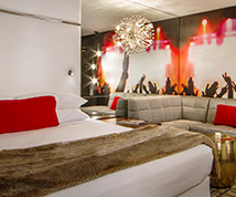 suite with white linens, brown blanket, mural pained on the wall, and a seating area with a tan couch