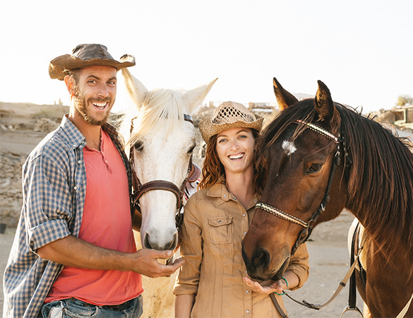 a woman and a man each one feeding two horses in an arid field