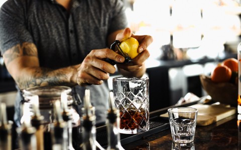 bartender peeling lemon zest onto glass