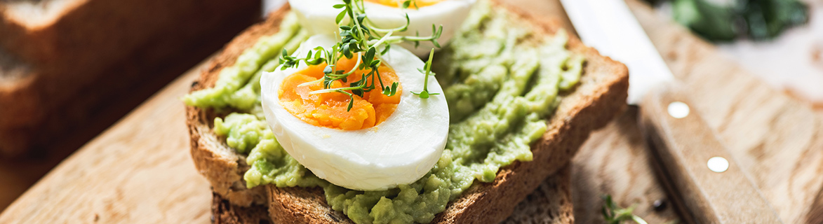 avocado on a piece of toast with a hardboiled egg on top garnished with fresh herbs