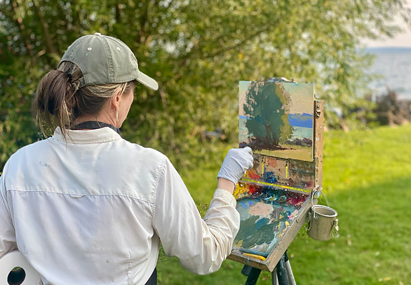 View of a woman painting a landscape on a canvas outdoors