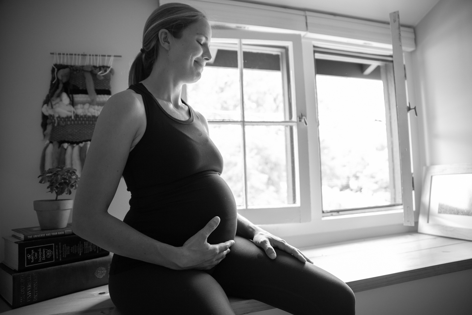 black and white image of a pregnant lady sitting while she touches her stomach 
