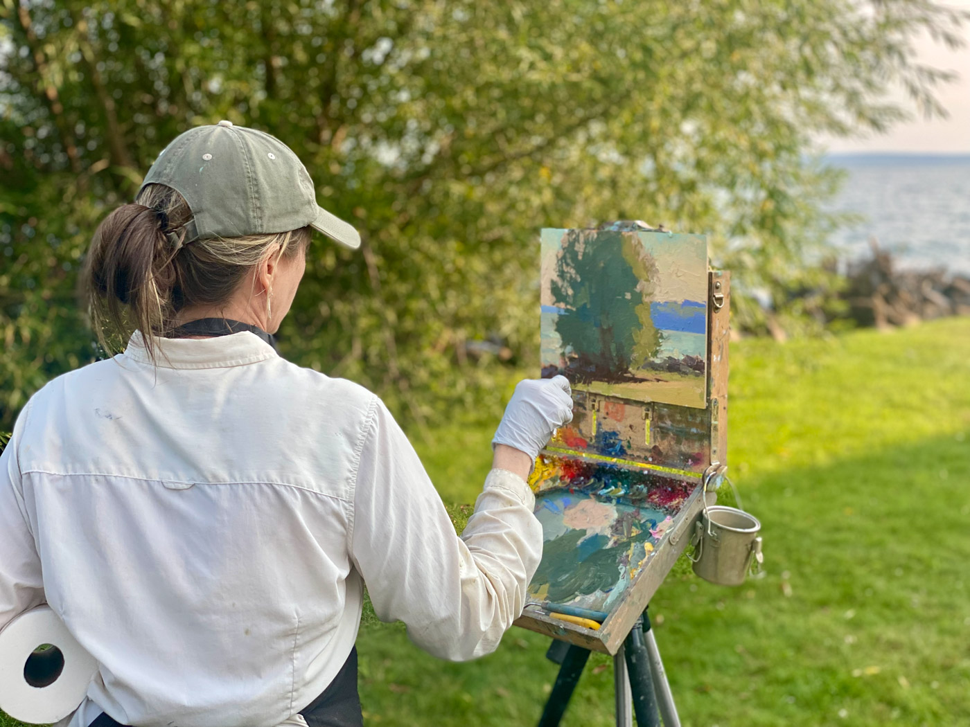 Back view of a woman painting a landscape on canvas outdoors