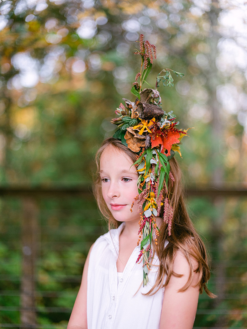 a little girl with a variation of leaves and flowers that are piled on top of her head