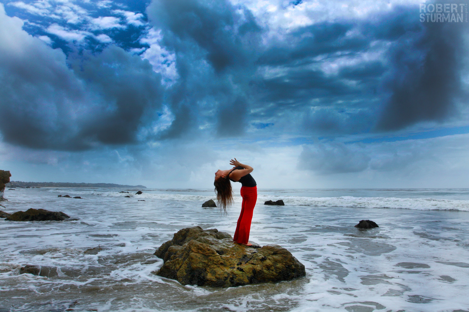 A woman standing on a rock in the middle of the ocean doing a yoga pose
