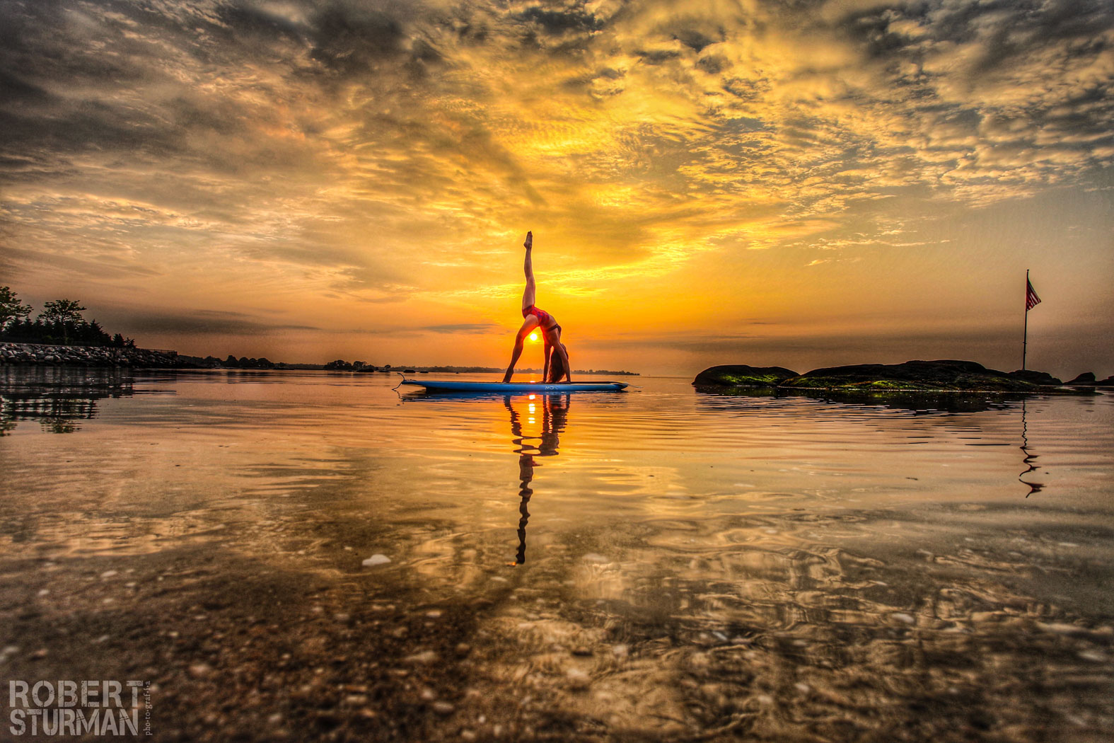 View of a woman on a paddle board doing a yoga pose on sunset
