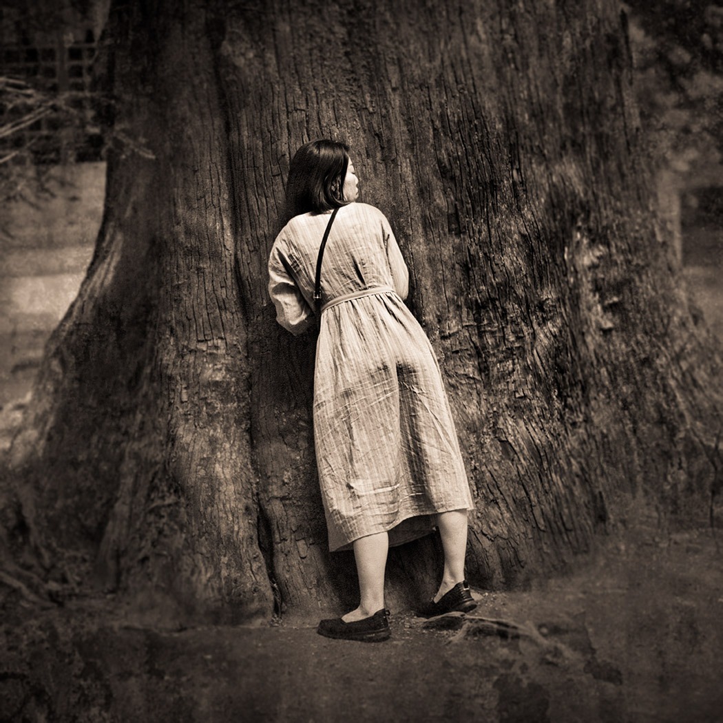 A sepia portrait of a woman leaning on a tree