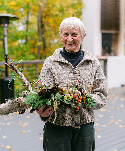 a lady holding a branch that has flowers and green leaves growing out of it