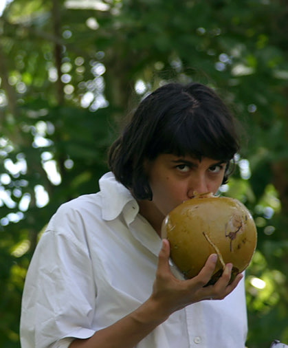 woman wearing a white shirt is drinking something from the coconut