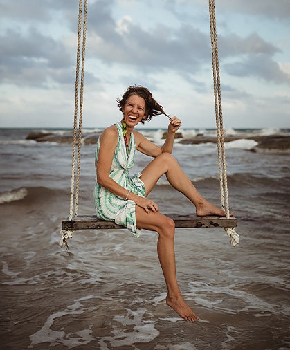 smiled woman sitting on a swing at the beach 
