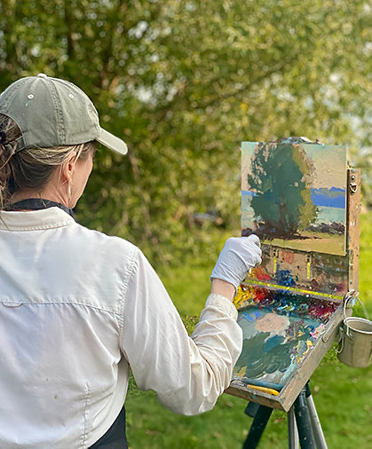 Back view of a woman painting a landscape on canvas outdoors
