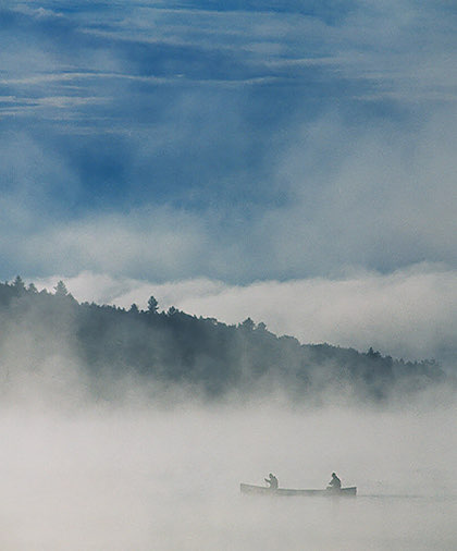 Picture of a boat surrounded by fog and some green trees on the background 
