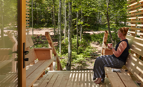 View of a woman drinking a cup of tea and relaxing outside a cabin