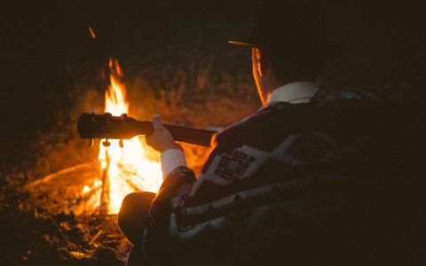 man playing guitar in front of a bonfire