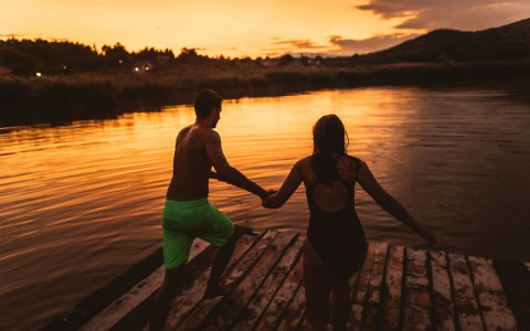 girl and boy jumping off a dock into a lake at sunset