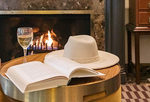 hat, book, and wine by the fire