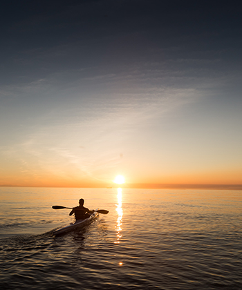 A man on a kayak at the sea at sunset