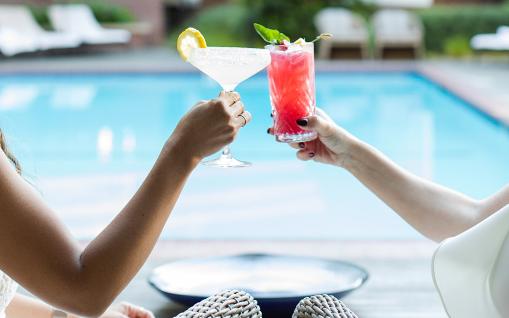 View of two people toasting with tropical cocktails next to the pool