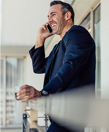 man smiling and holding a glass of drink while he es having a call