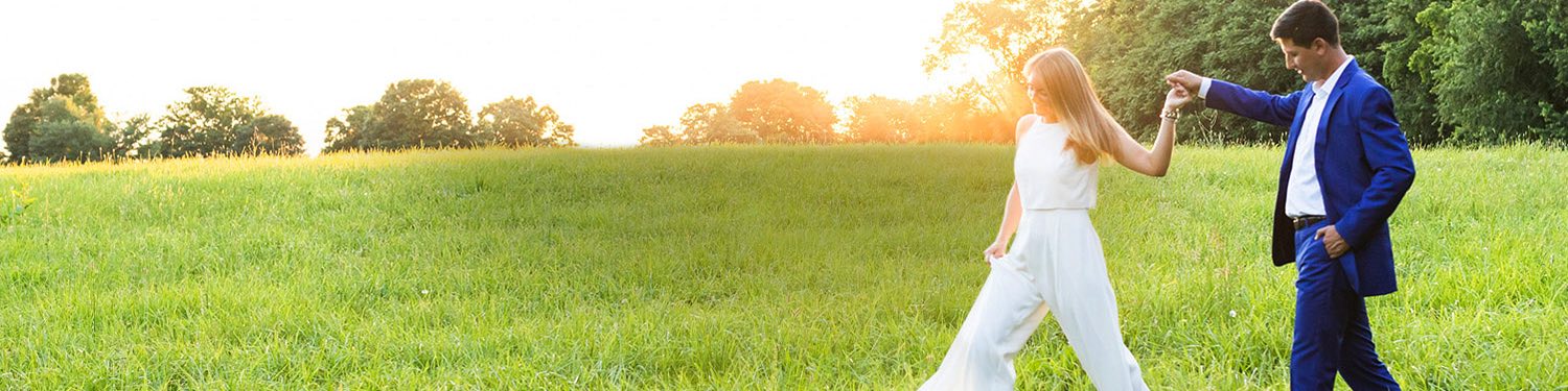 Couple holding hands as they walkthrough green grass hills