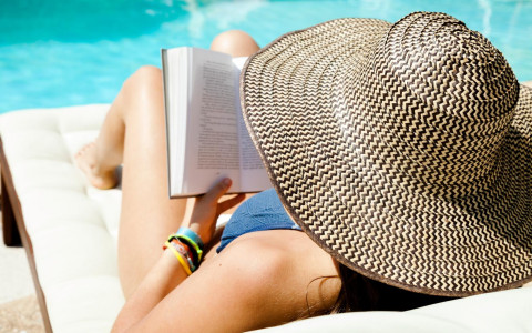 woman wearing a wide had laying by the pool reading a book
