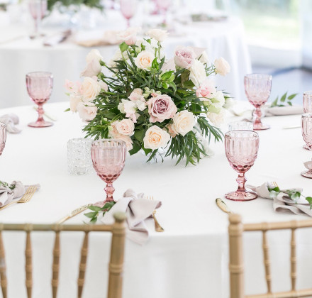 wedding table set with pink wine glasses, white tablecloth, gold chairs, and floral centerpieces