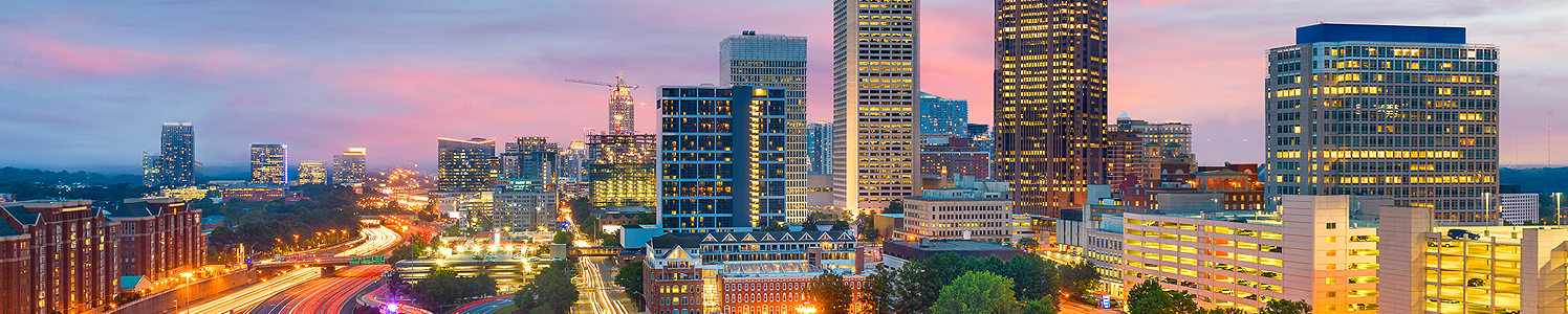 downtown atlanta city buildings lit up at dusk with a purple and pink sky