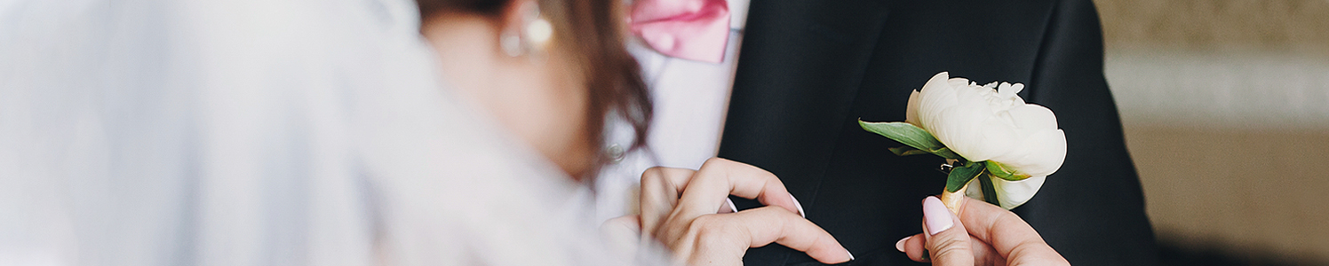 close up of a bride pinning a flower on the groom's suit