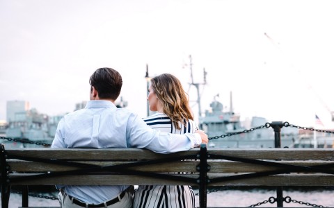 couple sitting on a bench that are near the boats at the port