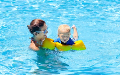 mom helping her child to learn how to swim in the pool