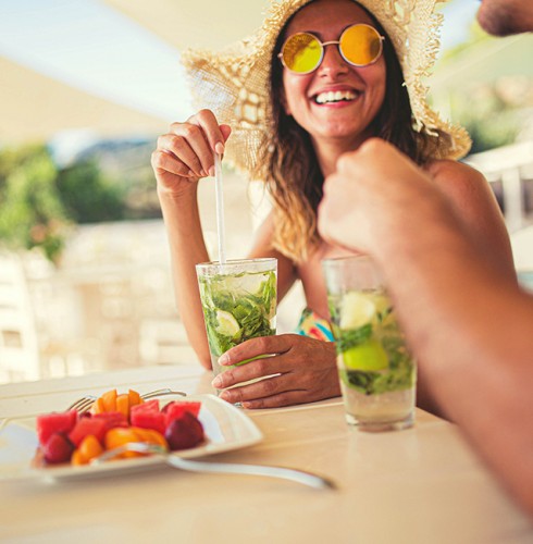 a woman wearing hat and sunglasses smiling and drinking a cocktail