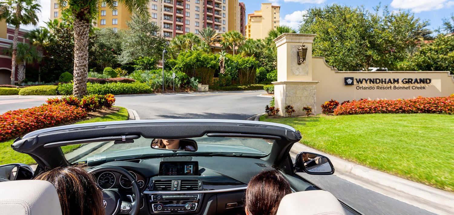 women driving a convertible car up to the entrance of the hotel