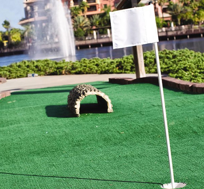 mini golf course with white pin flag and fountain in background