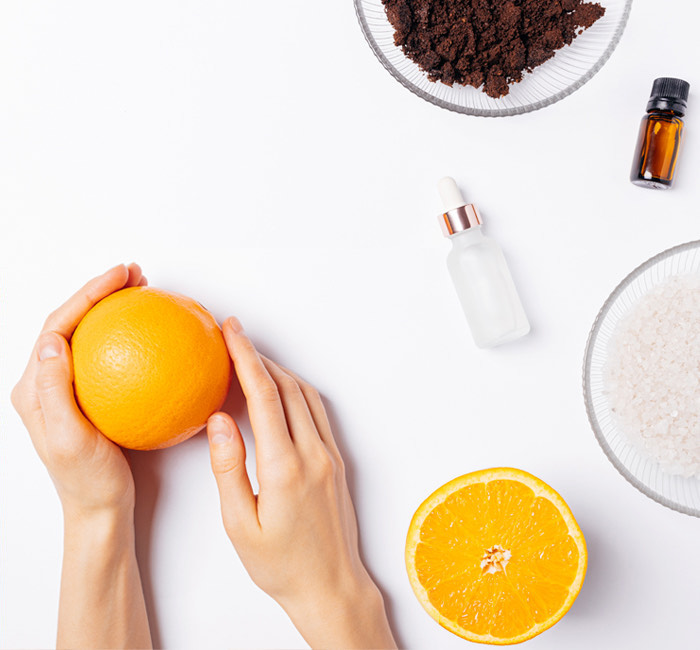 a pair of hands holding a orange with skin care products at the side