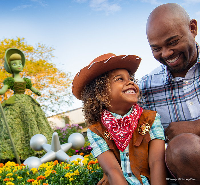 a father and his child smiling and happy at the toy story portion of the park in disney world