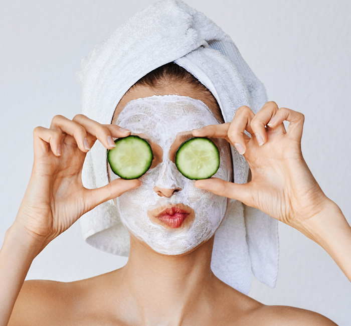 girl with a white mask and a towel in the hair with two cucumbers in the hands