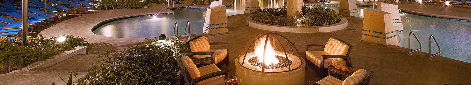 Pool area at night with glowing fire pit surrounded by lounge chairs