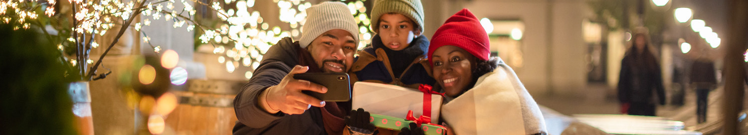 a family taking a selfie together in warm clothes with lights in the background for the holidays