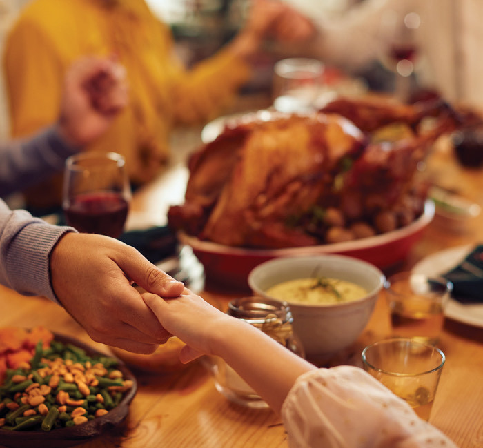 a father and daughter holding hands at the dinner table for a holiday feast with the family
