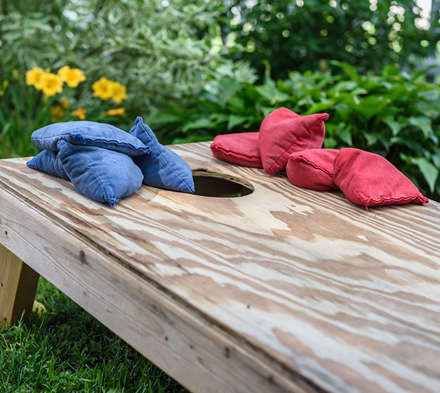 a cornhole game with red and blue rice bags sitting on grass with yellow flowers in the background