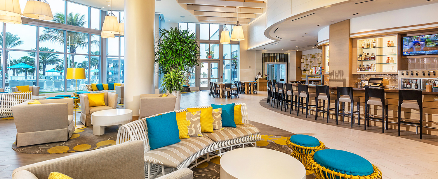 Lobby with wicker seating, colorful pillows & bar in the back